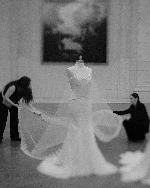 Wedding dress strapless wedding dress on a mannequin with beaded neckline and cathedral veil, long satin train spread in an indoor gallery hall