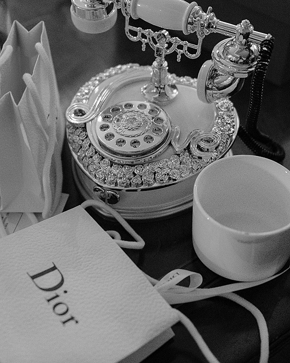 Wedding flat lay with bridal details flat lay featuring a vintage rotary phone, white ribbon, designer gift bag, coffee cup, and napkin on a tabletop