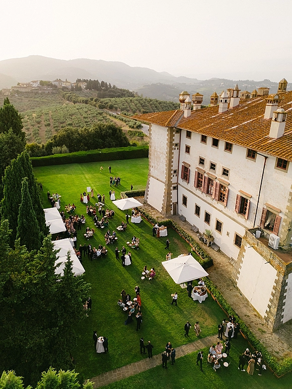 Outdoor wedding reception with wedding cocktail hour setup, cocktail tables under white umbrellas on a manor lawn with mountain views