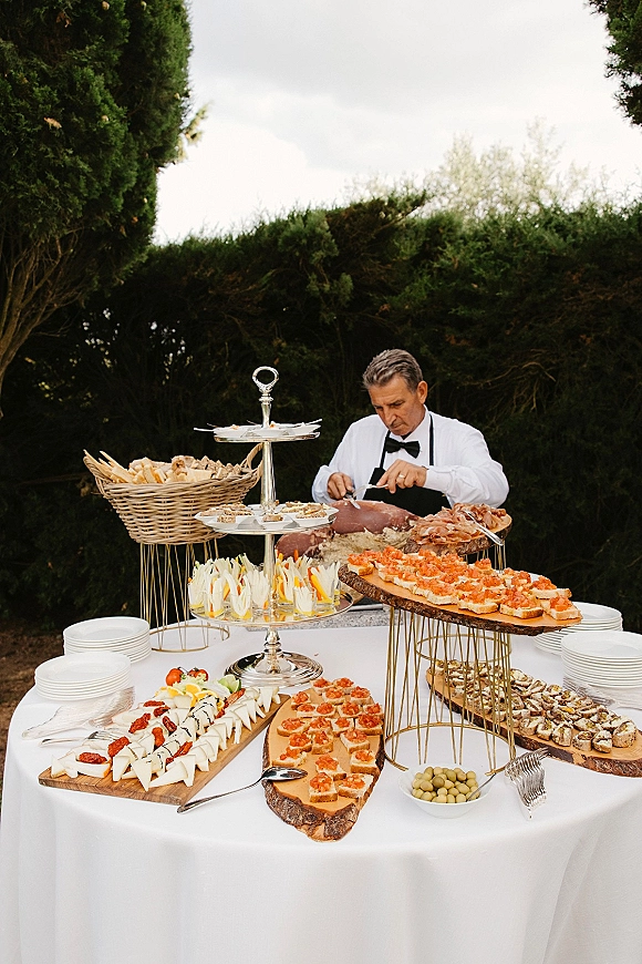 Cocktail hour spread with wedding cocktail hour food, featuring charcuterie, cheeses, baguettes and canapés on white linen outdoors