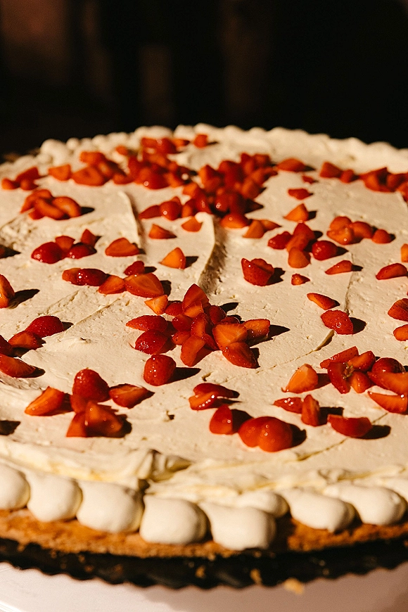 Wedding cake with white frosting and strawberry topping, bordered piping on a cake stand against a dark background