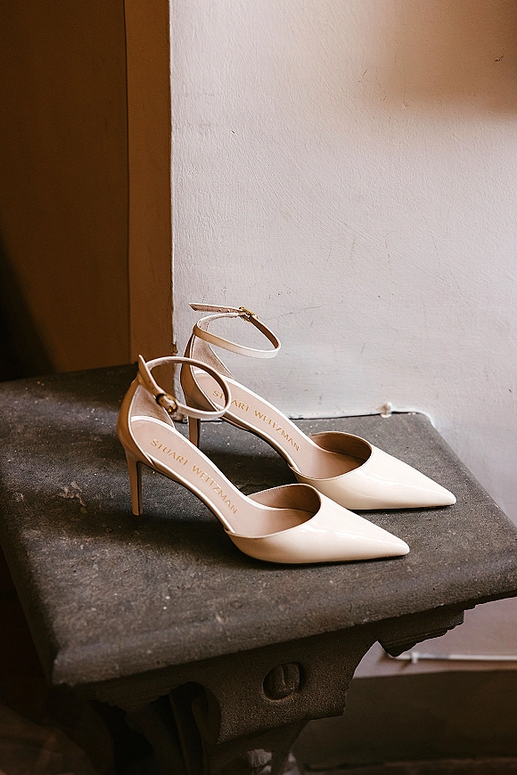 Bridal shoes in nude wedding heels style, pointed-toe patent stiletto with ankle strap on a stone ledge in window light
