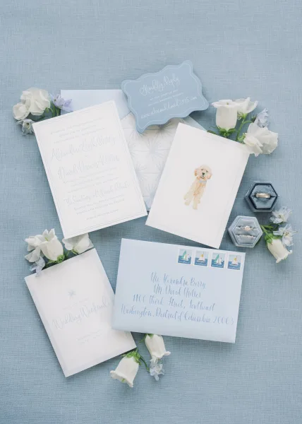 Wedding invitation suite featuring blue wedding invitations with postage stamps, styled on blue linen fabric.