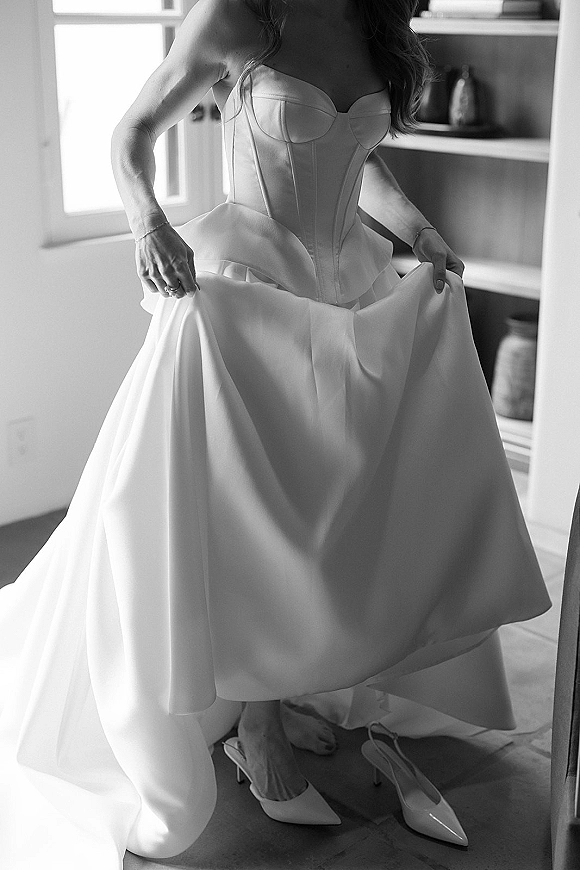 Wedding dress with a corset wedding dress bodice and strapless satin neckline, held in window light beside shelving at home interior