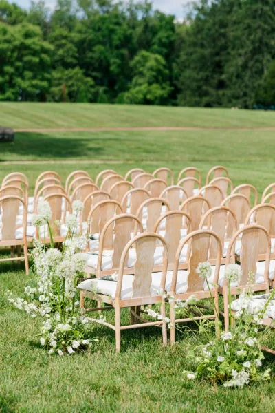 Ceremony seating arranged for an outdoor ceremony setup, rows of chairs flanking a central aisle lined with aisle flowers.