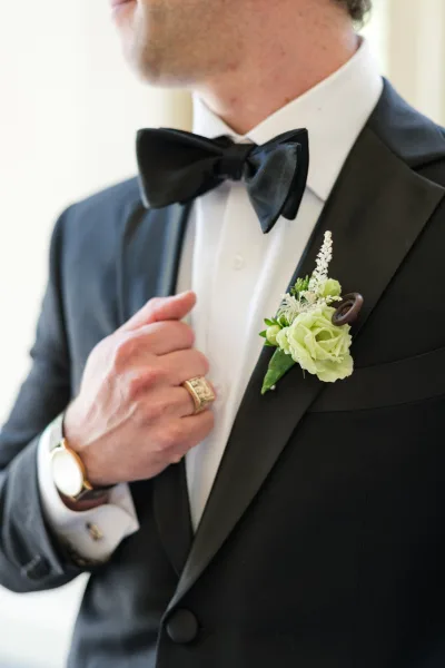 Boutonniere close-up of a groom boutonniere, green and white florals with greenery pinned to a black tuxedo lapel.
