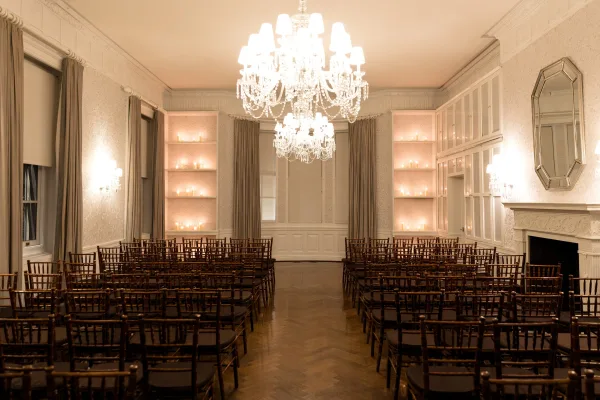 Ceremony setup for an indoor wedding ceremony with crystal chandeliers illuminating a classic ballroom of paneled walls and herringbone wood floors.