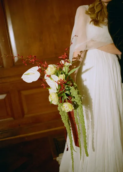 Wedding bouquet styled as a cascading bridal bouquet, with sculptural anthurium blooms, shown indoors against warm wood paneling and hardwood floors.