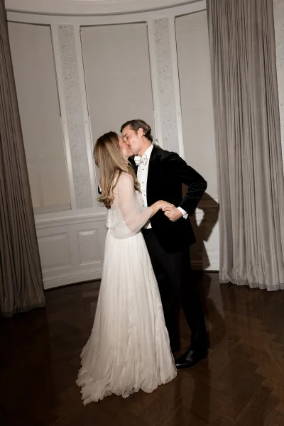 Wedding kiss portrait capturing a slow dance kiss as the bride in long sleeves and the groom embrace by curtained windows