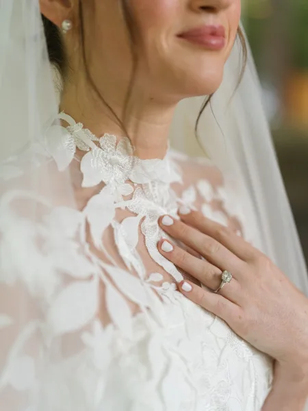 Bridal gown details showcasing a lace wedding dress bodice with floral appliqué, bride’s hand adorned with an engagement ring resting on the lace.