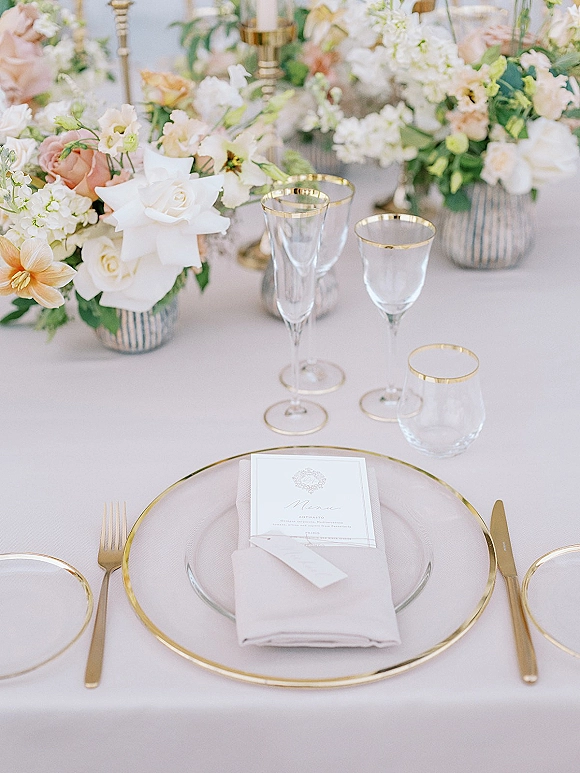 Reception tablescape with wedding place setting, gold-rim charger plate, blush napkin, menu card, pastel roses in striped vases and taper candles