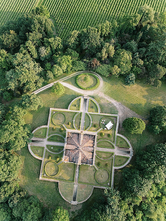 Garden wedding venue aerial wedding venue view with a white event tent, manicured hedges and topiary shrubs beside vineyard rows and lawn