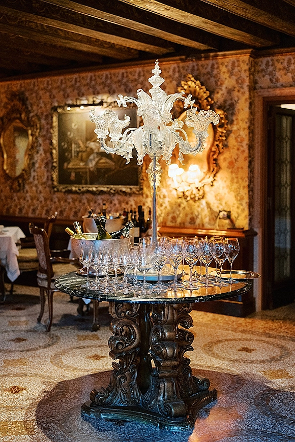 Champagne station wedding champagne bar on a marble pedestal table with coupe glasses, bottles on ice, and a crystal candelabra in a vintage room