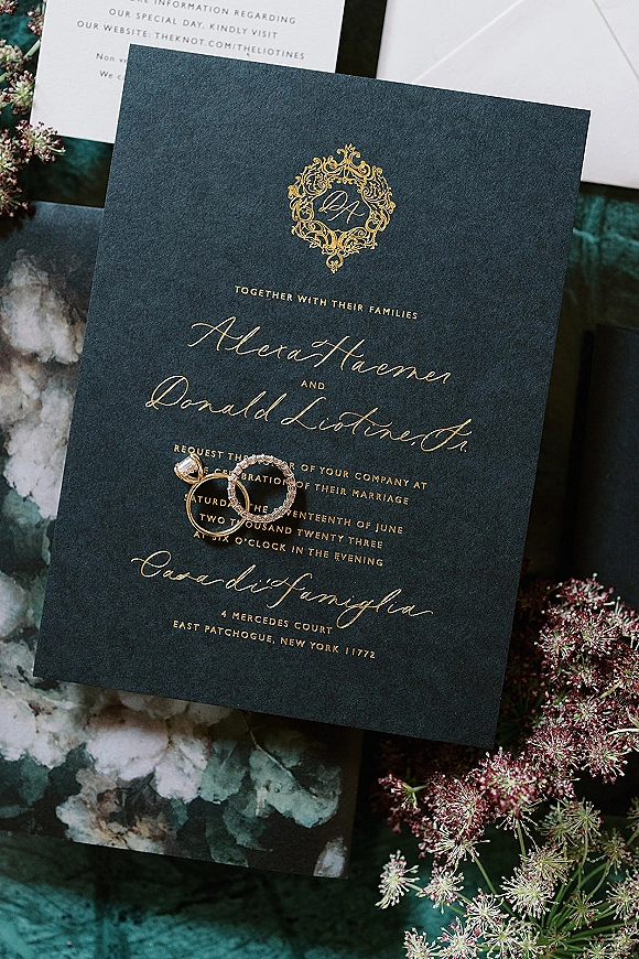 Wedding invitation with navy and gold foil calligraphy, monogram crest, rings on the suite, on marbled paper over a dark surface