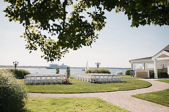 Outdoor ceremony setup with waterfront wedding ceremony chairs lining a gravel aisle, floral markers and greenery by the harbor view