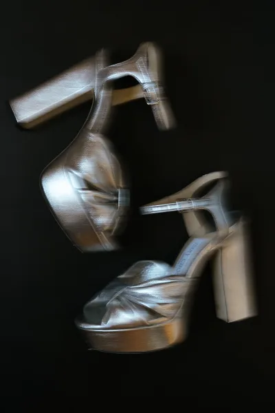 Bridal shoes with metallic finish and bow detail, platform heels and ankle strap posed against a sleek black background