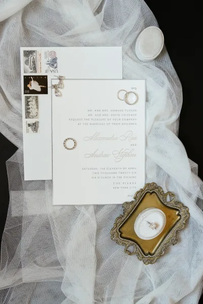 Invitation suite wedding invitation flat lay with rings, wax seal, vintage stamps and earrings arranged on an ornate tray over dark fabric