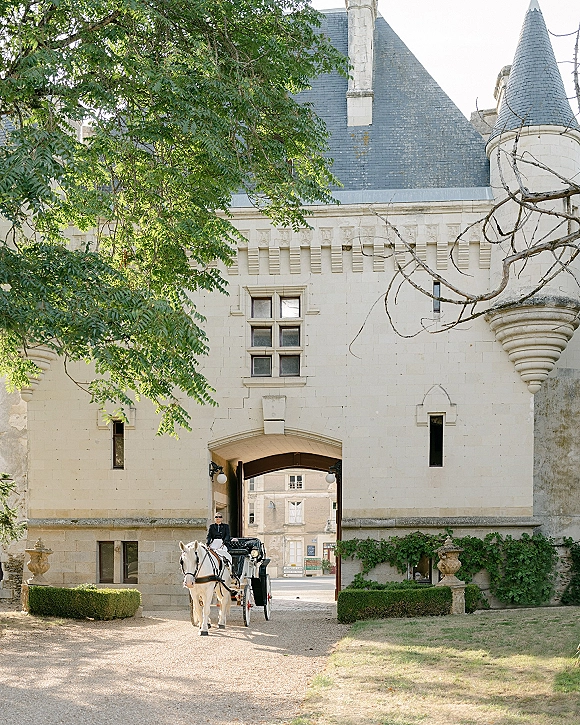 Wedding carriage arrival with a horse and carriage wedding entrance at an ivy-covered stone castle gate on a gravel driveway