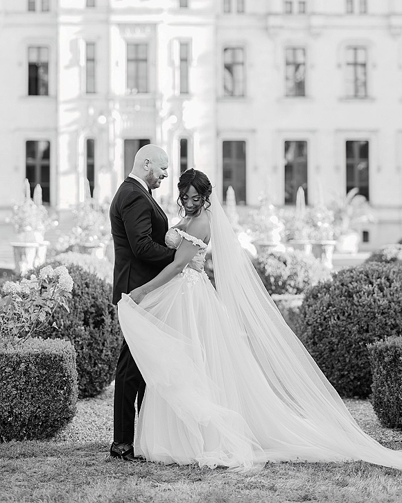 Couple portrait in a black and white wedding portrait, bride looking over shoulder as groom embraces her in a formal estate garden setting