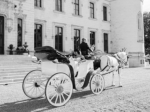 Wedding carriage exit with bride and groom in a horse drawn wedding carriage, white horse waiting by castle steps and tall windows