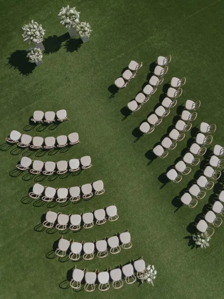 Ceremony seating layout with outdoor ceremony seating in a curved arrangement of cushioned chairs and white floral urns on green lawn