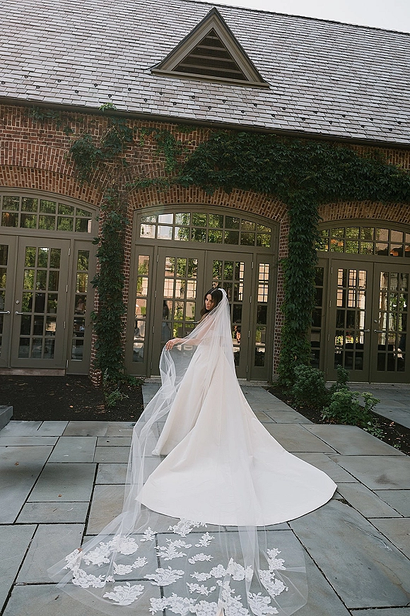 Bridal portrait of a cathedral veil bride in a strapless wedding dress, looking over her shoulder by ivy on brick arches and glass doors