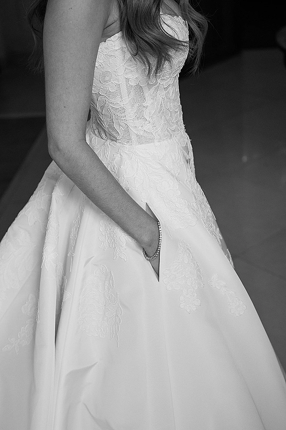 Wedding dress with lace wedding dress bodice and floral appliqué, strapless neckline and full skirt, shown in a dark interior background