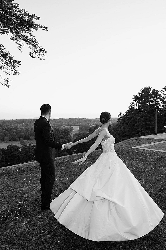 Couple portrait, black and white wedding portrait of bride and groom holding hands from behind on a hilltop overlooking valley and trees