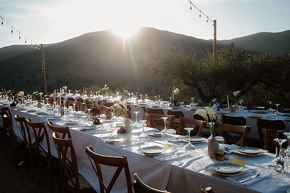 Reception tablescape at an outdoor wedding reception with long banquet tables, taper candles and calla lilies beneath string lights at sunset mountain view