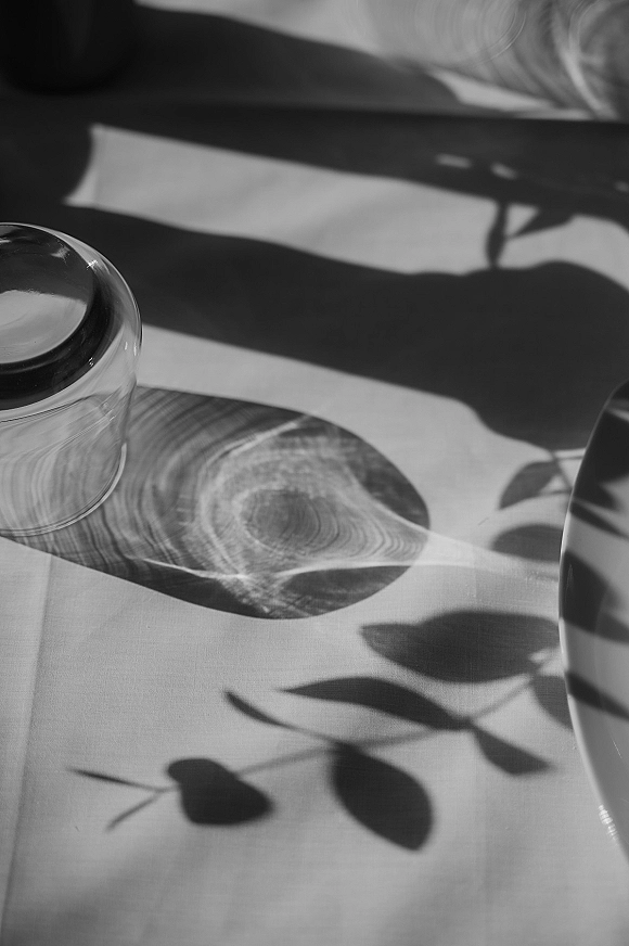 Wedding tablescape with a minimal wedding table setting featuring a glass tumbler, ceramic plate, and linen napkin in leaf-shadowed light
