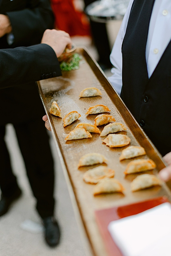 Wedding cocktail hour with passed hors d'oeuvres as a server in a vest offers dumplings on a tray to guests on outdoor pavement