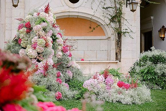 Wedding floral installation of hydrangea wedding flowers with baby's breath clouds and pink blooms, set against a stone facade with arched niche and lanterns