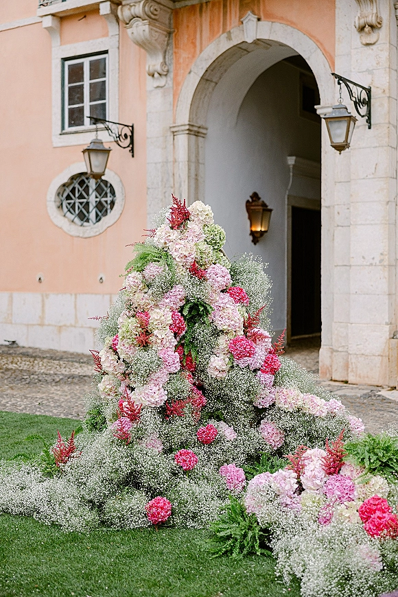 Wedding floral installation with hydrangea wedding flowers and baby's breath, spilling greenery and ferns at a stone arch courtyard entrance
