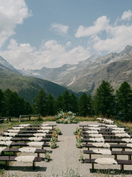 Mountain ceremony setup with outdoor ceremony decor and sheepskin throws draped across seating, set before a mountain range and evergreen trees.
