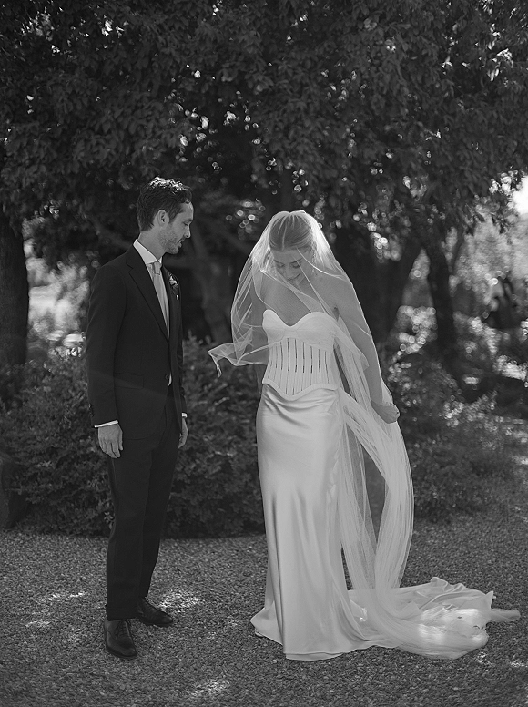 Couple portrait in black and white, bride in strapless gown with long veil and train beside groom in dark suit on a garden path