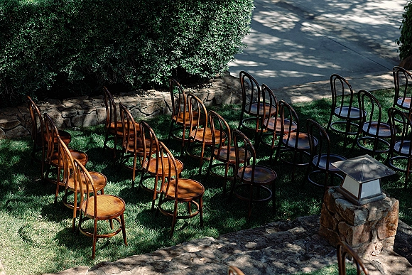 Ceremony seating with outdoor wedding chairs in neat rows on a grass lawn, mixed wood chairs facing a stone pillar lantern in tree shade