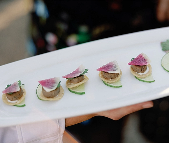 Wedding appetizers arranged as passed hors doeuvres on a white platter with cucumber, radish, microgreens, and tart shells at an indoor reception