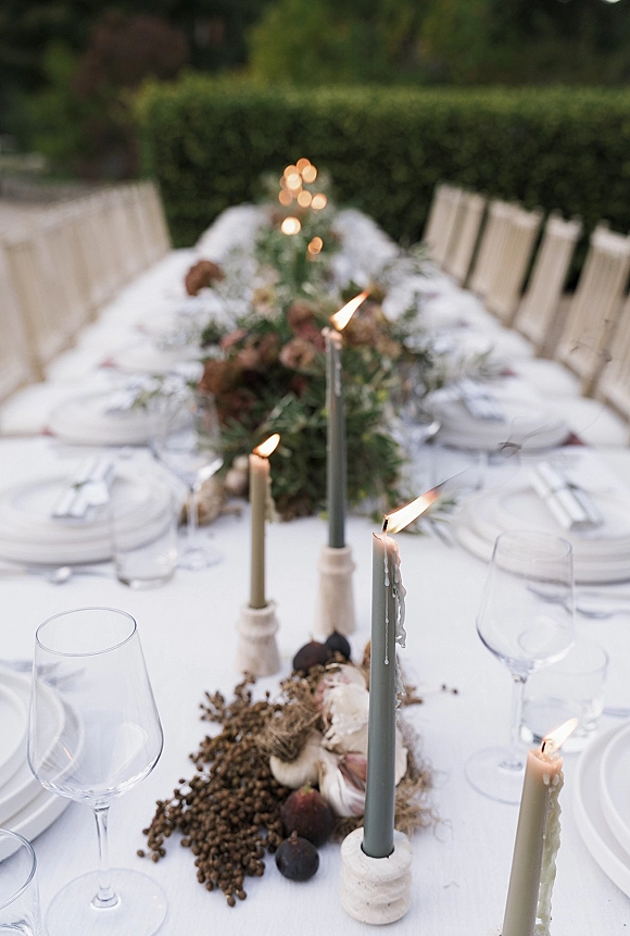 Reception tablescape with outdoor wedding tablescape details, taper candles, greenery garland, figs and florals on a long table by hedges and trees