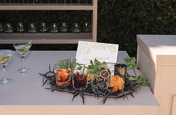 Wedding cocktail bar with signature cocktail wedding menu, martini glasses and olives on a white counter against a hedge wall backdrop