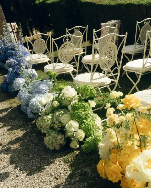 Ceremony aisle decor for garden ceremony seating with hydrangeas lining a gravel path, framed by a garden hedge and gate.