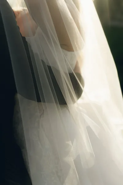Bridal veil close-up reveals tulle veil detail and soft sheer layers against a black tuxedo accent, framed by garden greenery.