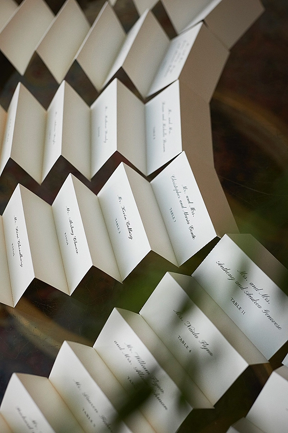 Wedding place cards with calligraphy place cards in black ink on folded white tent cards arranged neatly on a glass tabletop