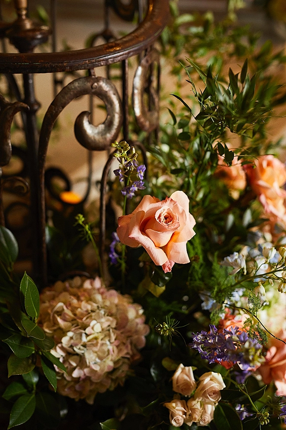 Wedding floral arrangement of peach rose wedding flowers with hydrangea and greenery draped along a wrought iron indoor staircase in warm light