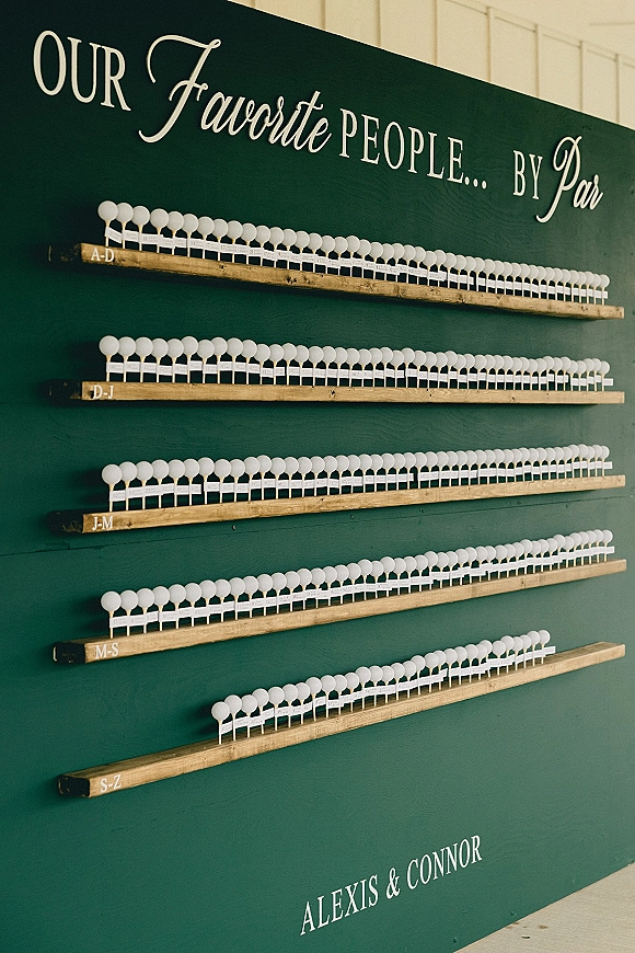 Wedding seating chart with escort card display on wooden shelves, printed lettering and white place markers against a white tent wall