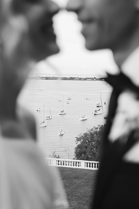 Wedding kiss as the bride and groom share a waterfront silhouette kiss by a stone balustrade with sailboats on the harbor behind them