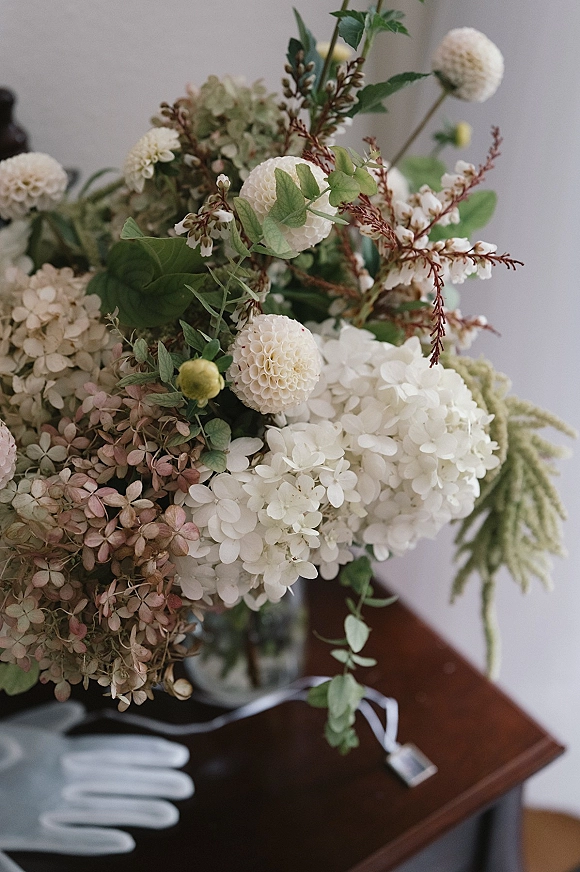 Bridal bouquet of white dahlias and hydrangea bridal bouquet with lush greenery, tied with ribbon in a vase on a table by a white wall