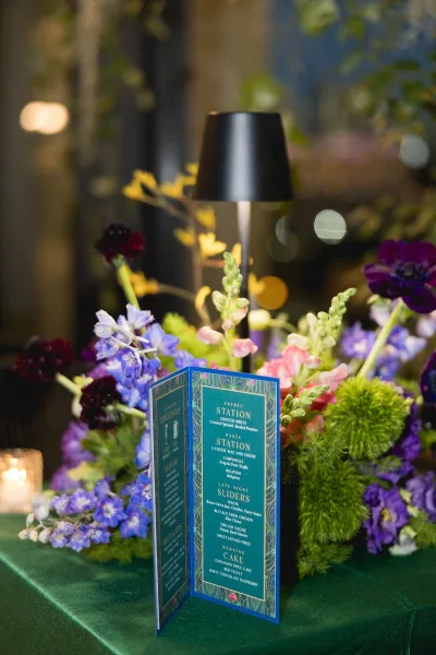 Wedding menu card with art deco wedding stationery styling, folded on velvet linen beside floral centerpiece and candle votive in dim bokeh lighting