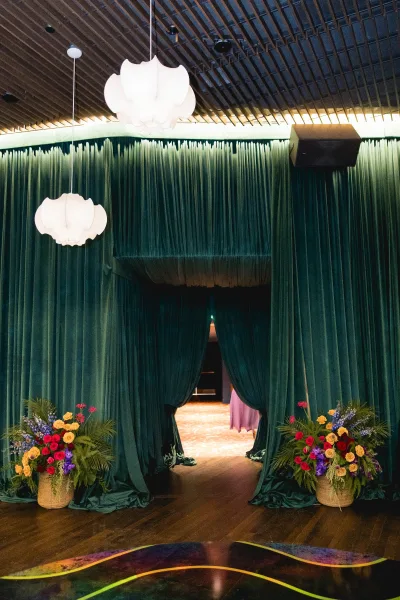Wedding entrance decor with draped wedding entrance in emerald green curtains, floral baskets, and pendant lights framing a doorway under wood slats
