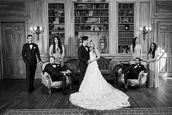 Wedding party portrait of bride in strapless lace gown and groom with tuxedoed attendants in a wood-paneled library with bookshelves