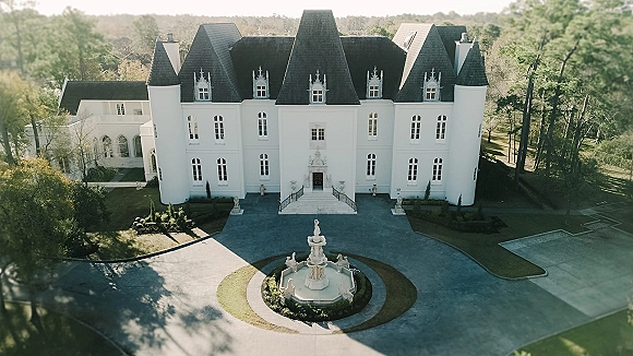 Wedding venue exterior of a castle wedding venue with turrets and arched windows, grand staircase, and fountain by a circular driveway and lawn